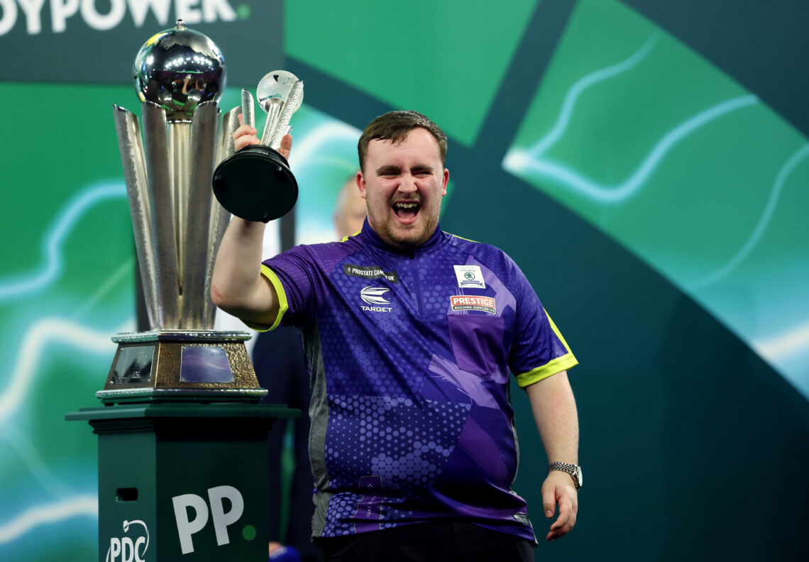 Luke Littler holding a dartboard after winning a championship.